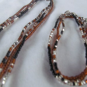 Puede incluir: Un conjunto de dos collares hechos de cuentas negras, marrones y plateadas. El collar m&aacute;s largo es un colgante y el collar m&aacute;s corto es una pulsera.