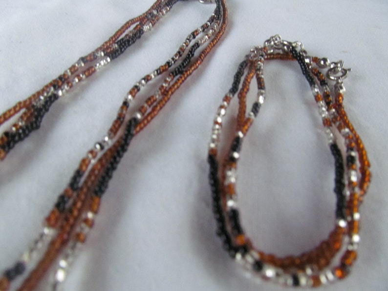 Puede incluir: Un conjunto de dos collares hechos de cuentas negras, marrones y plateadas. El collar m&aacute;s largo es un colgante y el collar m&aacute;s corto es una pulsera.
