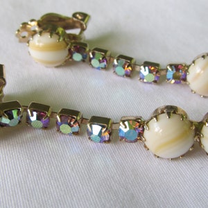 May include: A pair of gold tone clip-on earrings with iridescent rhinestones and white shell-like beads.