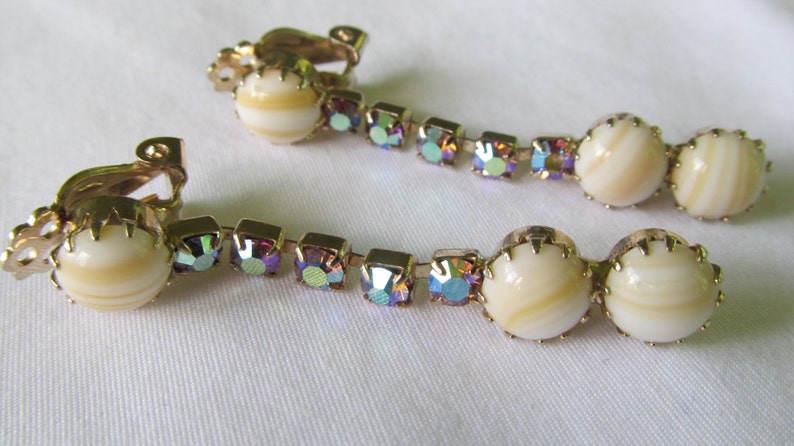 May include: A pair of gold tone clip-on earrings with iridescent rhinestones and white shell-like beads.