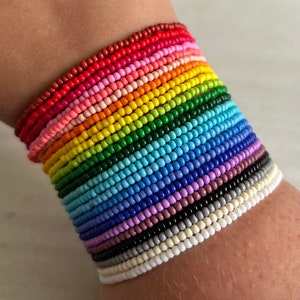 May include: A rainbow beaded bracelet made of small, colourful beads. The bracelet is layered with different colours, creating a vibrant and colourful look.