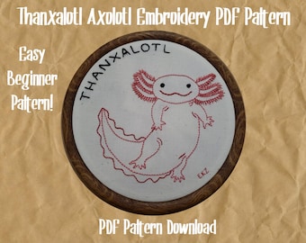 May include: Embroidery pattern for an axolotl, a type of salamander, in a wooden embroidery hoop. The pattern is titled "Thanxaloti Axolotl Embroidery PDF Pattern" and includes the text "Easy Beginner Pattern!" and "PDF Pattern Download".