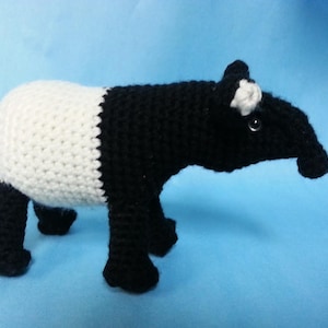 Puede incluir: Un animal de peluche tejido a crochet que se asemeja a un tapir. El animal es negro y blanco con un hocico largo y orejas pequeñas.