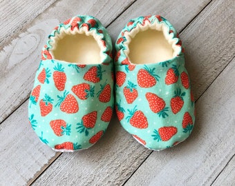 May include: A pair of baby slippers with a light blue background and a red strawberry pattern.