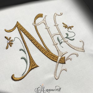 May include: Embroidered letter N with a gold and white floral design. The letter is in a script font and the flowers are stylized with small white beads for centers.