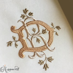 Może przedstawiać: Haftowany monogram litery "D" w kolorze złotym i białym z kwiatowymi zdobieniami.