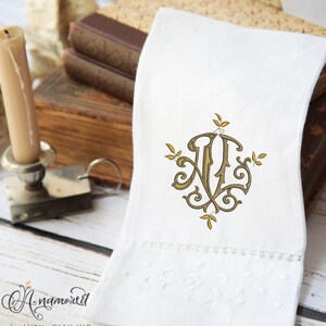 May include: White linen hand towel with an embroidered monogram in gold and brown. The towel features a decorative border and the text "A Namored" in cursive script.