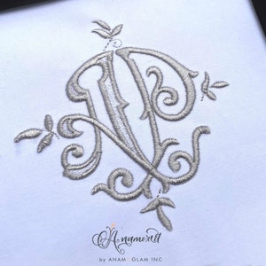 May include: A silver embroidered monogram of the letters "N" and "D" with decorative flourishes. The monogram is on a white background.