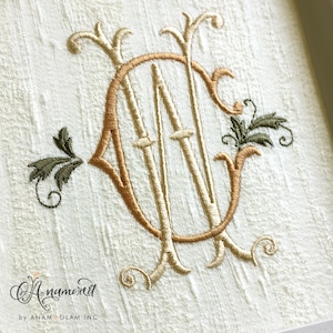 May include: Embroidered monogram art with the letters "AN" in a vintage style. Gold and tan thread is used on textured, off-white fabric. The design includes decorative flourishes and leaves, creating an elegant, classic appearance. The artwork is framed.