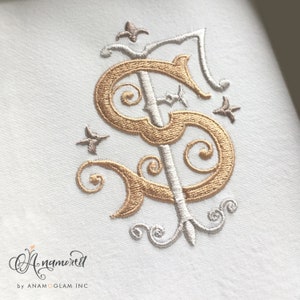May include: Gold and silver embroidered monogram with a decorative flourish. The monogram is the letter "S" with a decorative flourish.