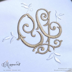 May include: A gold embroidered monogram with a decorative floral design. The monogram is in a script font and the flowers are white.