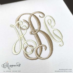 Pode incluir: Monograma bordado em fio bege claro e castanho claro sobre fundo branco. As letras entrelaçadas, provavelmente iniciais, apresentam uma escrita clássica e elegante. O design é de Anamored. Etsy.com.