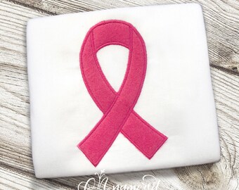 Puede incluir: Una cinta rosa en una camiseta blanca. La cinta es un símbolo de concienciación sobre el cáncer de mama.
