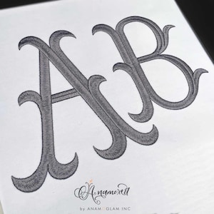 May include: A monogram embroidery design featuring the letters "A" and "B" in a stylized, cursive font. The letters are gray and are embroidered on a white background.