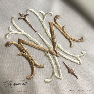 May include: A monogram with the letters "M" and "N" embroidered in gold and white thread on a white fabric background.