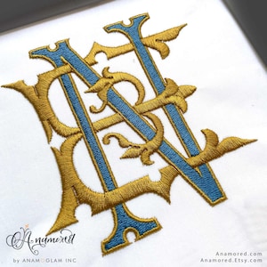 May include: Embroidered monogram in gold and blue thread on white fabric. The intertwined letters appear to be "AN". The design has ornate flourishes and is likely for a custom project. The Etsy shop name "Anamored" is in the bottom left corner.
