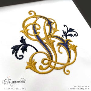 May include: Embroidered monogram in gold and navy blue on a white background. The design features ornate, intertwined letters with floral accents. The text "A.namored" is in a script font at the bottom, with "by ANAMOGLAM INC" below it.