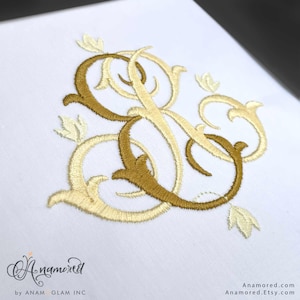 Może przedstawiać: Haftowany monogram z literami "S" i "G" splecionymi ze sobą, ze stylizowanym wzorem kwiatowym w kolorze złotym i kremowym.