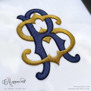 May include: Embroidered monogram in navy blue and gold thread on a white background. The intertwined letters, possibly initials, are stylized with decorative flourishes. The design is likely for personalization or embellishment.