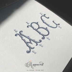 May include: Embroidered letters "ABC" in a decorative script font with silver embellishments on a white background. The letters are in a cursive style with flourishes and swirls.