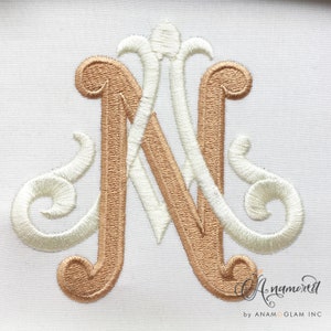 Może przedstawiać: Monogramowa litera „N” w ozdobnym, ozdobnym kroju pisma. Litera jest wyszyta w jasnobrązowym kolorze na białym tle z tkaniny. Litera jest obwiedziona białym kolorem.