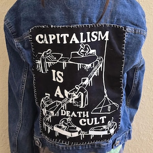 May include: A denim jacket with a black patch sewn on the back. The patch features a graphic of people working on an assembly line with the text "Capitalism is a Death Cult".