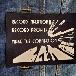 May include: Black and white patch with the text "Record Inflation, Record Profits, Make the Connection" and a graphic of a city street.