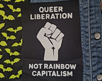 May include: A black patch with white text that reads "Queer Liberation" and "Not Rainbow Capitalism". A white raised fist is in the center of the patch.