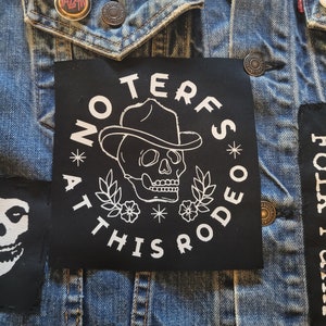 Peut inclure: Patch brodé noir et blanc avec un crâne portant un chapeau de cowboy et le texte "No Terfs At This Rodeo".