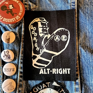 Pode incluir: Patch preto e branco com um design de bota e o texto "GOODNIGHT" e "ALT-RIGHT". A bota tem as letras "A" e "E" em círculo no lado.