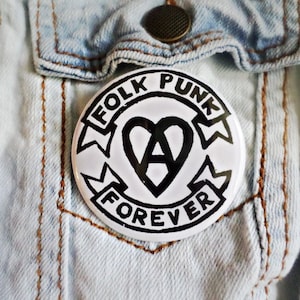 May include: A white button with black text and a heart design. The text reads "Folk Punk Forever".