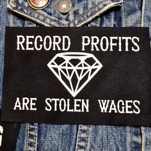 May include: Black and white patch with the text "Record Profits Are Stolen Wages" and a diamond graphic.