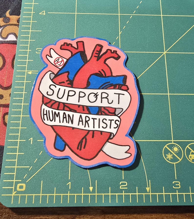 Op de afbeelding: Een sticker met een gestileerd anatomisch hart in rood en blauw, met een banner met de tekst "SUPPORT HUMAN ARTISTS" in zwarte letters. De sticker heeft een roze achtergrond en een blauwe omtrek.