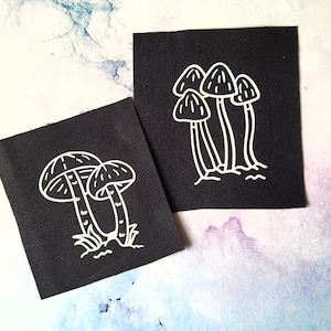 May include: Two black fabric patches with white outlines of mushrooms. One patch features three mushrooms with stems and caps. The other patch features two mushrooms with stems and caps.