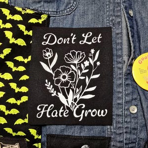 Puede incluir: Parche de tela negro con texto blanco y diseño floral. El texto dice "No dejes que el odio crezca".