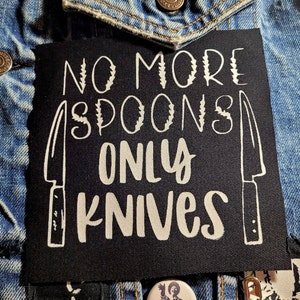 May include: Black patch with white text that reads "No More Spoons Only Knives" with a knife graphic on each side.