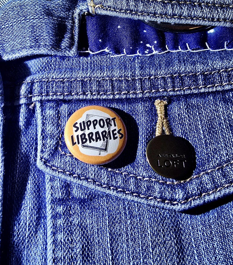 Puede incluir: Una chaqueta vaquera azul con un bot&oacute;n que dice "Support Libraries" y un bot&oacute;n negro con el texto "Ann Taylor LOFT" en &eacute;l.
