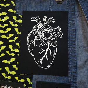 May include: A black patch featuring a white anatomical heart design. The heart illustration is detailed with veins and arteries. The patch is likely for clothing or accessories, adding a unique, edgy aesthetic.