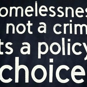 May include: A dark blue background with white text that reads "homelessness is not a crime its a policy choice."