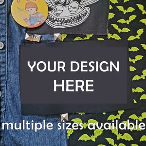 Może przedstawiać: Czarna dżinsowa kurtka z naszywkami, w tym kreskówkowym potworem, wzorem zielonych nietoperzy i pustą naszywką z napisem "YOUR DESIGN HERE". Tekst "multiple sizes available" jest nadrukowany pod pustą naszywką.