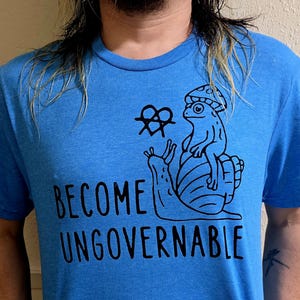 May include: A blue t-shirt with a black graphic of a frog riding a snail. The graphic also includes a heart with an anarchy symbol. The text "Become Ungovernable" is printed below the graphic.