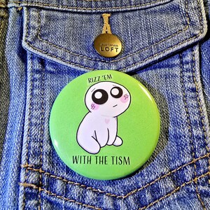 May include: A green button with a white cartoon character and the text "Rizz 'em with the tism" on a denim jacket.