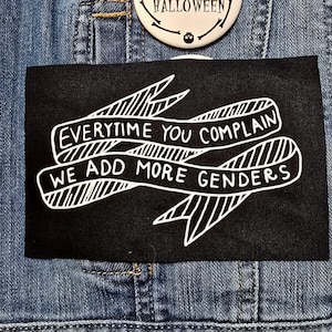 May include: Black iron-on patch with white text that reads "Everytime you complain we add more genders".