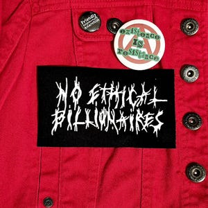 May include: A red denim jacket with silver buttons and three pins. One pin reads "Friendly Neighborhood Anarchist", another says "existence IS resistance" with an anarchy symbol, and a third patch reads "NO ETHICAL BILLIONAIRES" in white text.