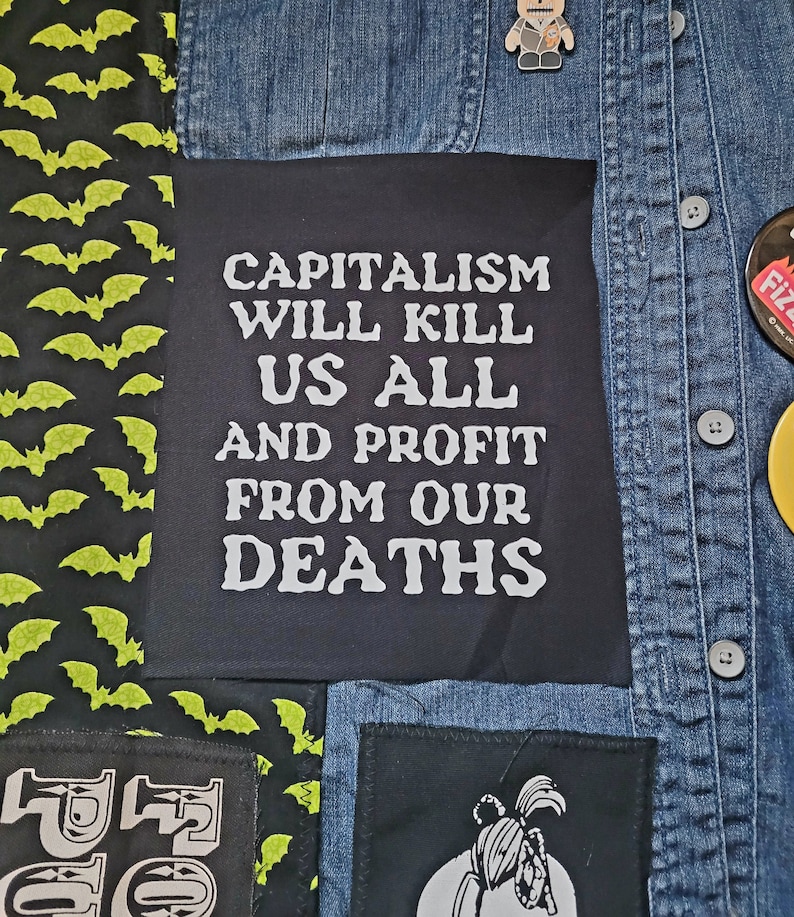 May include: A denim jacket with various patches, including a black patch with white text that reads "Capitalism Will Kill Us All And Profit From Our Deaths".