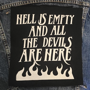 May include: Black square patch with white text that reads "HELL IS EMPTY AND ALL THE DEVILS ARE HERE." The patch features a flame design at the bottom. The patch is pinned to a denim jacket.