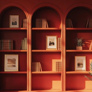 May include: A set of three arched bookshelves with a red finish. The shelves are filled with books, framed pictures, and plants. The shelves are against a red wall.
