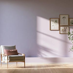 Può includere: Una poltrona grigio chiaro con un cuscino rettangolare color malva poggia su un pavimento in legno chiaro in una stanza con pareti color lavanda. Una pianta verde in vaso si trova accanto e quattro stampe botaniche incorniciate sono a parete.