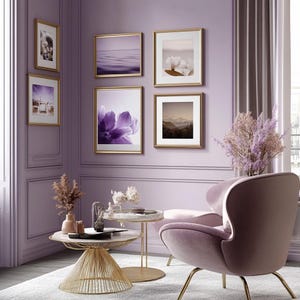 May include: A living room with a purple wall and a pink armchair. There are five framed pictures on the wall, including a purple flower, a mountain range, and a cotton plant. There is a gold metal coffee table with a white marble top.