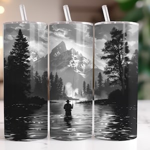 May include: A set of three stainless steel tumblers with a black and white landscape design. The design features a fisherman in a river, mountains, and trees. Each tumbler has a clear straw.